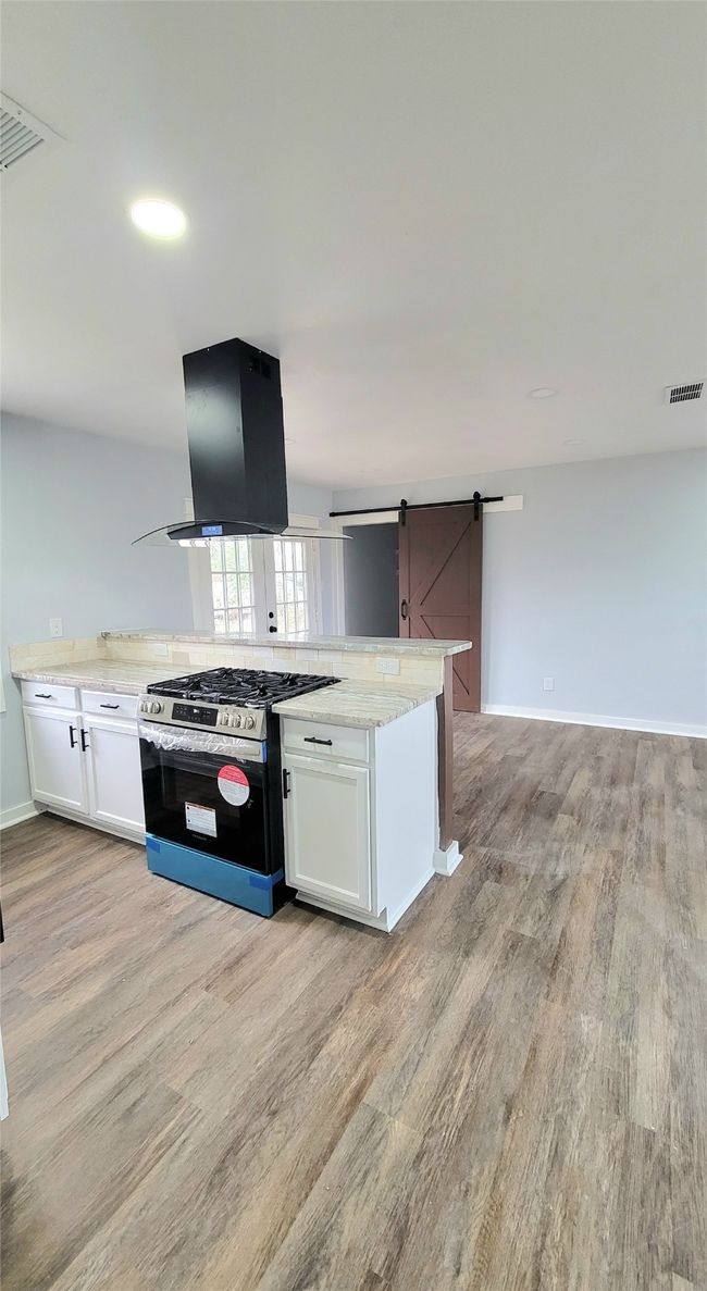 Kitchen with stainless steel gas stove, a barn door, visible vents, island range hood, and open floor plan | Image 4