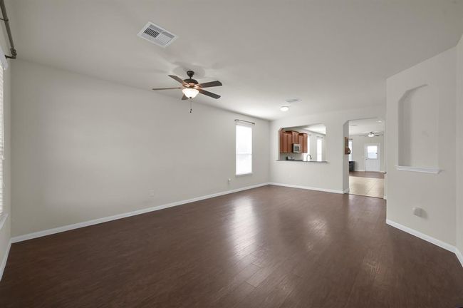This spacious living area features hardwood floors, a ceiling fan, and neutral walls. It opens to a kitchen with a pass-through window, creating a seamless flow for entertaining. | Image 5