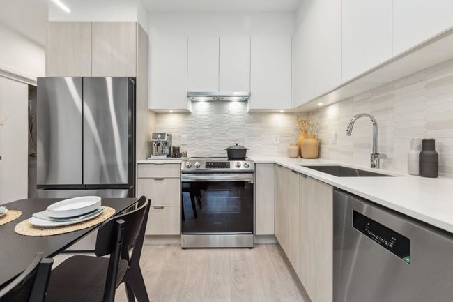 Kitchen featuring stainless steel appliances, light countertops, modern cabinets, a sink, and light wood-type flooring | Image 5
