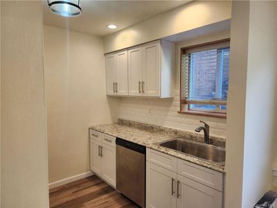 Kitchen with sink, stainless steel dishwasher, backsplash, white cabinetry, and hardwood / wood-style flooring | Image 2