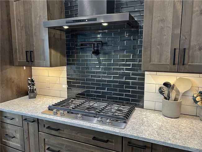 Large gas cooktop, custom black stainless vent hood over dark glass subway tiles | Image 11
