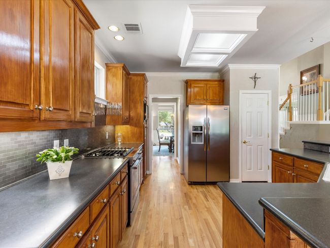 Kitchen featuring stainless steel appliances, dark countertops, brown cabinetry, crown molding, and recessed lighting | Image 10
