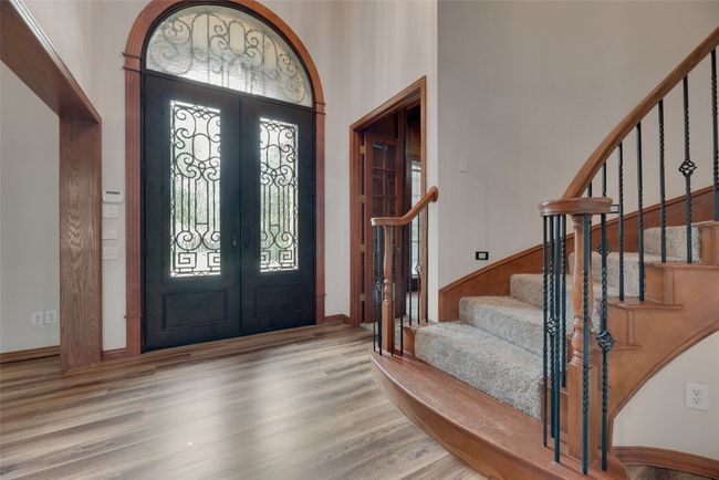 Double iron door entry is flanked by an office with double doors on one side and a library or sitting room on the other before reaching the sweeping staircase. | Image 4
