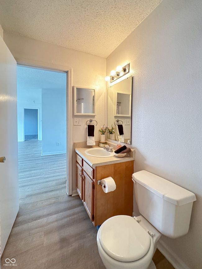 bathroom featuring a textured wall, toilet, vanity, and wood finished floors | Image 12