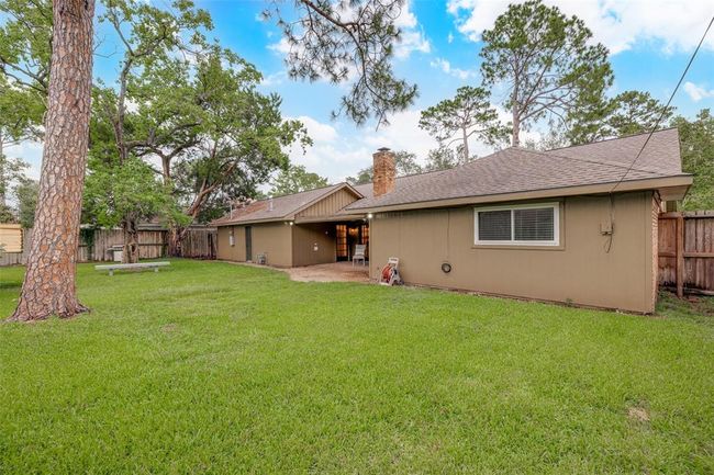 Spacious backyard with lush green grass and mature trees. The house features a single-story, rustic exterior with a chimney and a fully fenced perimeter, offering privacy and a wonderful outdoor space for entertaining family & friends. | Image 27