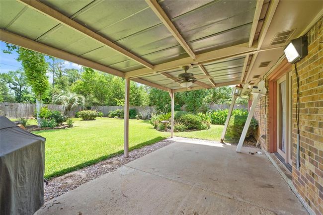 This photo showcases the covered patio with a ceiling fan, providing a shaded outdoor space. It overlooks a well-maintained backyard with lush greenery and a fence for privacy, perfect for relaxation or entertaining. | Image 26