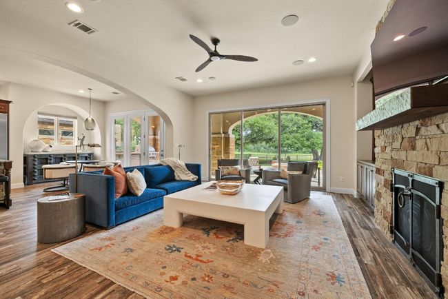 Living area with a stone fireplace, wood finished floors, ceiling fan, arched walkways, and recessed lighting | Image 7