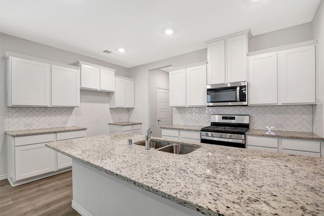 Kitchen featuring appliances with stainless steel finishes, white cabinetry, tasteful backsplash, light wood finished floors, and light stone counters | Image 5