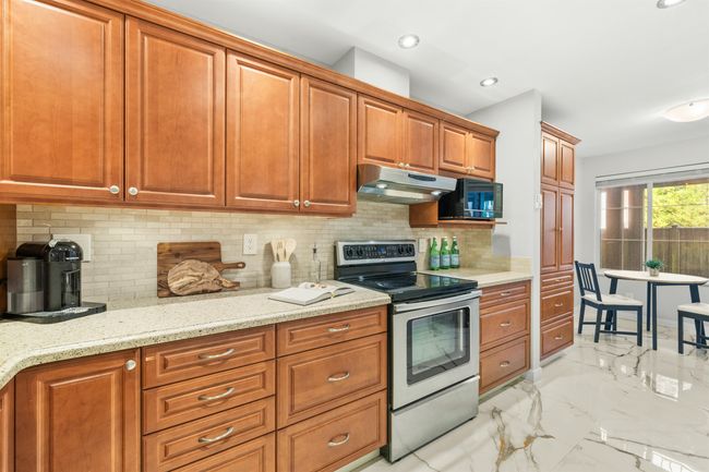 Kitchen with electric stove, marble finish floor, brown cabinetry, light stone countertops, and under cabinet range hood | Image 6