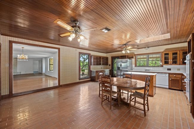Dining space featuring wooden ceiling, a ceiling fan, brick patterned flooring, a chandelier, and healthy amount of natural light | Image 11