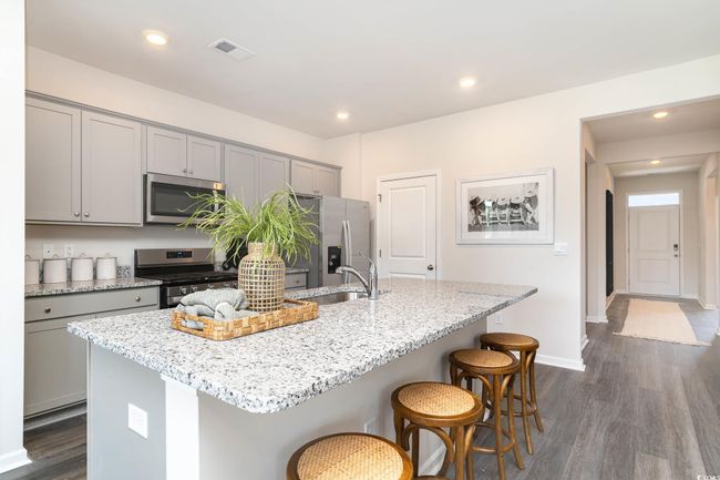 Kitchen with a kitchen island with sink, a breakfast bar, gray cabinets, appliances with stainless steel finishes, and dark wood-type flooring | Image 4