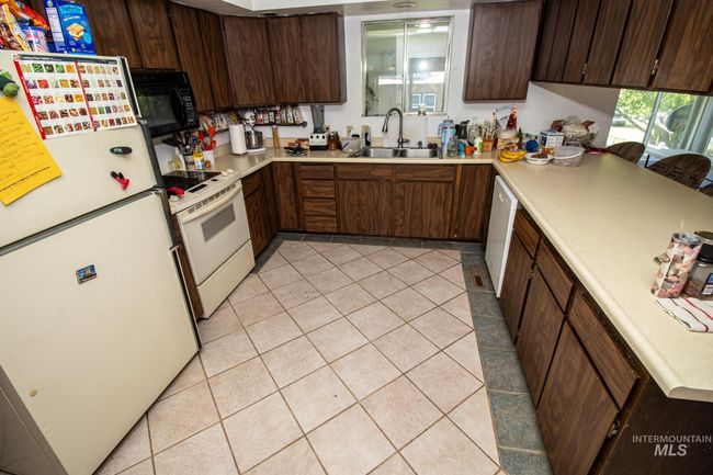 Kitchen with white appliances, light tile patterned flooring, light countertops, and dark brown cabinetry | Image 19