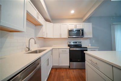 Kitchen featuring appliances with stainless steel finishes, white cabinets, backsplash, hardwood / wood-style flooring, and sink | Image 2