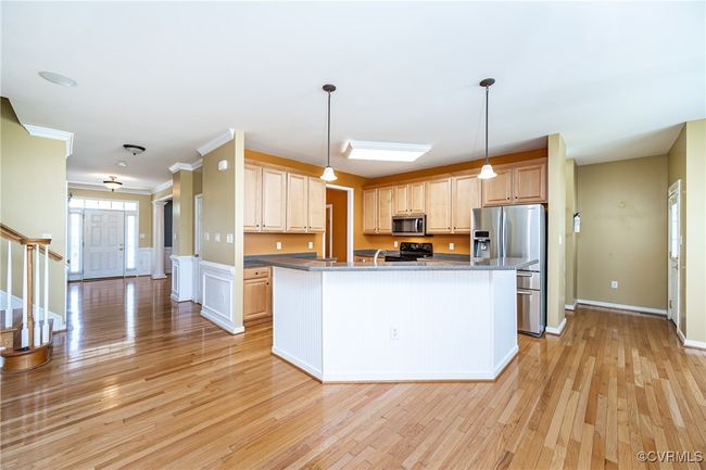Kitchen with stainless steel appliances, light wood-style floors, light brown cabinets, a center island with sink, and hanging light fixtures | Image 11