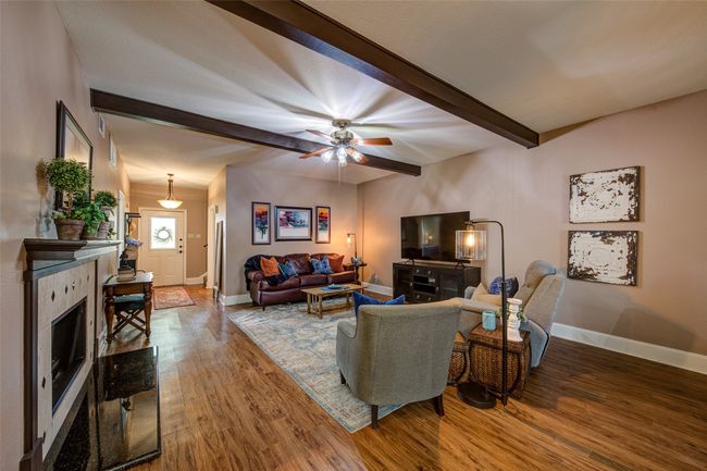 Living area with beam ceiling, wood finished floors, ceiling fan, and a fireplace | Image 7