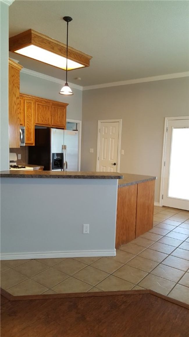 Kitchen featuring refrigerator with ice dispenser, stainless steel microwave, light tile patterned floors, a peninsula, and ornamental molding | Image 8