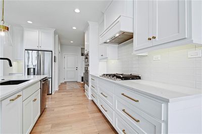 Kitchen with light wood-type flooring, custom exhaust hood, backsplash, stainless steel appliances, and decorative light fixtures | Image 2