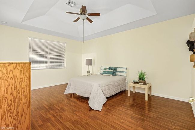 Bedroom featuring baseboards, a tray ceiling, visible vents, and wood finished floors | Image 15