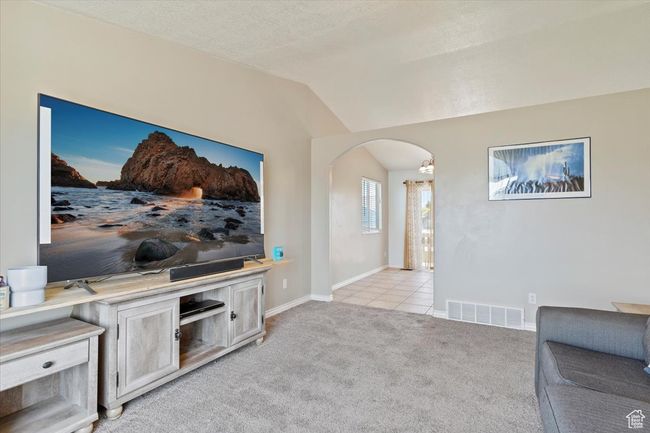 Living room with arched walkways, vaulted ceiling, baseboards, carpet, and tile floors. | Image 6