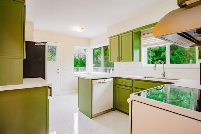 Kitchen featuring wall chimney range hood, light tile patterned flooring, white appliances, light countertops, and green cabinetry | Image 10