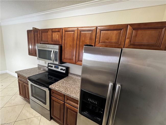 Kitchen featuring light tile patterned floors, stainless steel appliances, brown cabinetry, and crown molding | Image 16