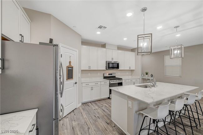 Kitchen with stainless steel appliances, a sink, light wood-style flooring, light stone counters, and white cabinetry | Image 24