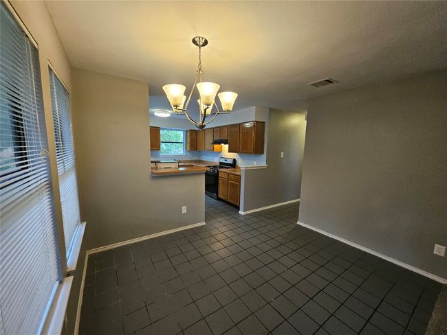 Kitchen with black gas stove, baseboards, visible vents, dark tile patterned flooring, and a notable chandelier | Image 11