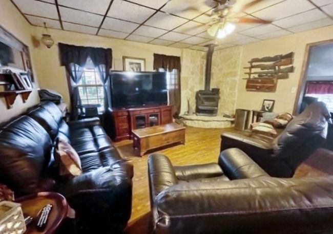Living area with wood finished floors, a paneled ceiling, ceiling fan, and a wood stove | Image 14