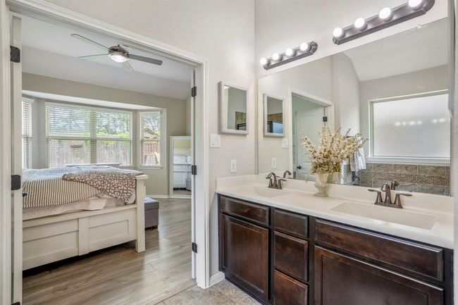 A close-up of the dual sinks reveals thoughtful details — the window’s soft light reflected in the mirror, and just to the left, the bay windows peek through the open double doors, tying the bathroom and bedroom together with warmth and natural light. | Image 24