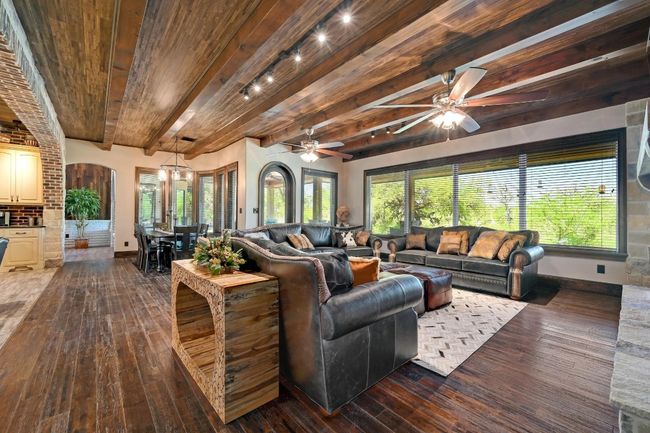 Living room featuring baseboards, arched walkways, beam ceiling, ceiling fan with notable chandelier, and dark wood-type flooring | Image 11