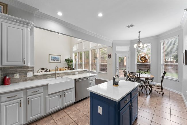 Kitchen with stainless steel dishwasher, light tile patterned floors, a chandelier, blue cabinets, and crown molding | Image 11