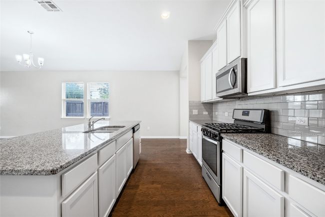 Kitchen featuring appliances with stainless steel finishes, backsplash, light stone countertops, and a chandelier | Image 15