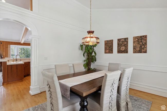 Dining room with arched walkways, light wood finished floors, a chandelier, a decorative wall, and a wainscoted wall | Image 7