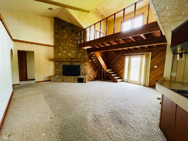 unfurnished living room with high vaulted ceiling, carpet, a fireplace, stairs, and baseboards | Image 9