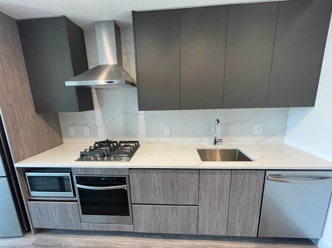 Kitchen featuring wall chimney range hood, a sink, appliances with stainless steel finishes, gray cabinetry, and modern cabinets | Image 12