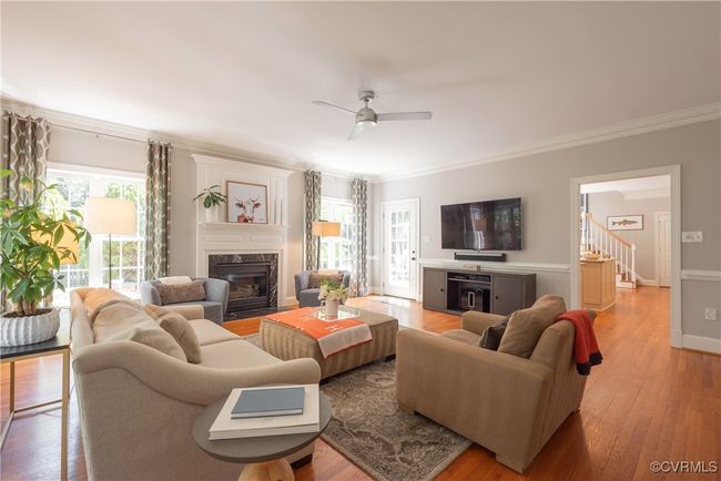 Living area featuring crown molding, ceiling fan, light wood-style flooring, stairs, and a premium fireplace | Image 11