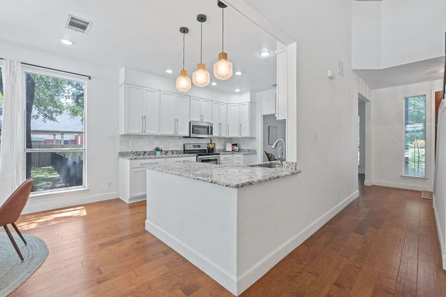 Kitchen featuring light stone countertops, appliances with stainless steel finishes, hardwood / wood-style flooring, white cabinets, and recessed lighting | Image 11
