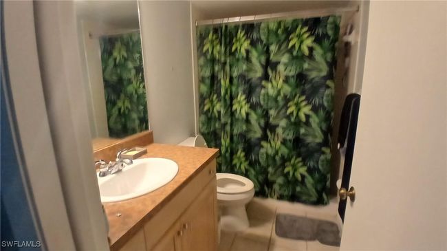 Bathroom with toilet, a shower with curtain, tile patterned floors, and vanity | Image 17