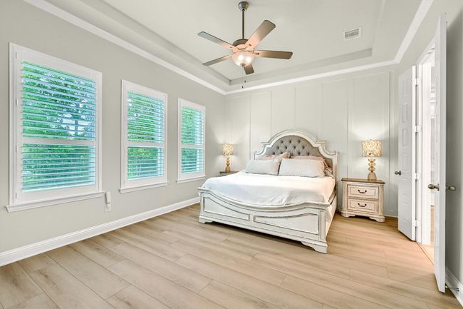Bedroom with a tray ceiling, light wood-style flooring, visible vents, and multiple windows | Image 17