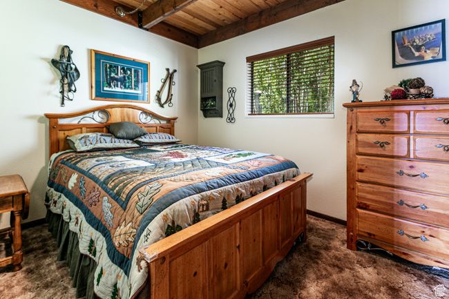 Bedroom with dark colored carpet and a wooden ceiling with exposed beams | Image 7
