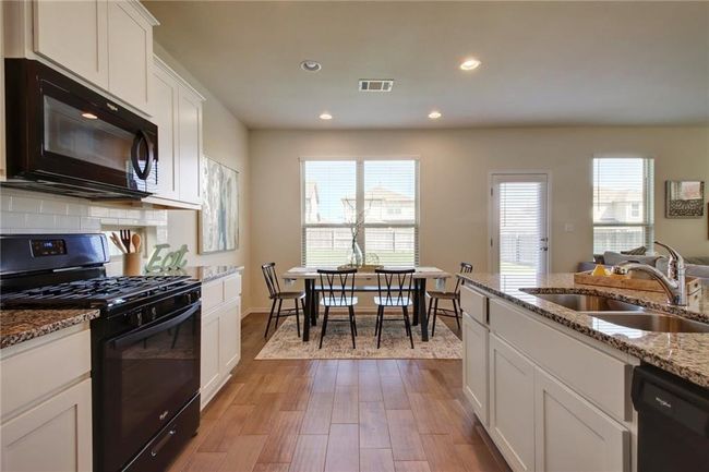 Kitchen with black appliances, light wood-style floors, white cabinets, recessed lighting, and light stone counters | Image 12