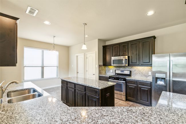 Kitchen with appliances with stainless steel finishes, a sink, decorative backsplash, light stone counters, and decorative light fixtures | Image 15