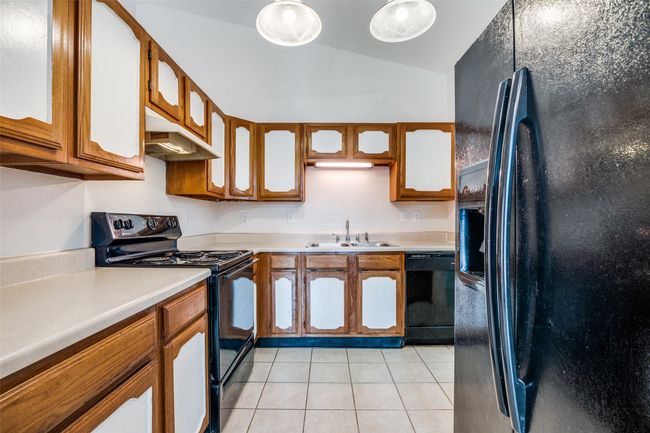 Kitchen featuring black appliances, under cabinet range hood, lofted ceiling, light countertops, and brown cabinetry | Image 12