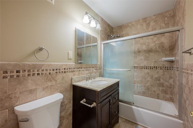 Full bath with combined bath / shower with glass door, toilet, tile walls, wainscoting, and vanity | Image 10