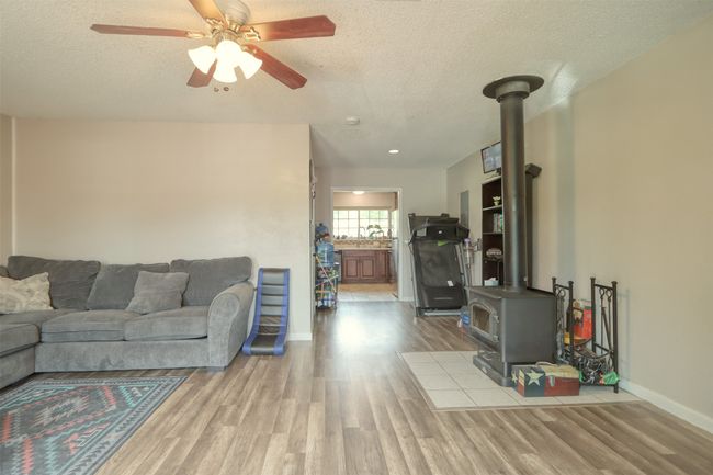 Living room featuring a wood stove, a textured ceiling, wood finished floors, and a ceiling fan | Image 24