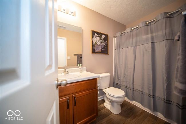 full bathroom with dark vinyl flooring with wood appearance, vanity, toilet, a textured ceiling, and a shower with curtain | Image 22