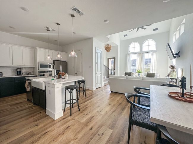 Kitchen with stainless steel appliances, a kitchen breakfast bar, light wood-style floors, a kitchen island with sink, and light countertops | Image 12