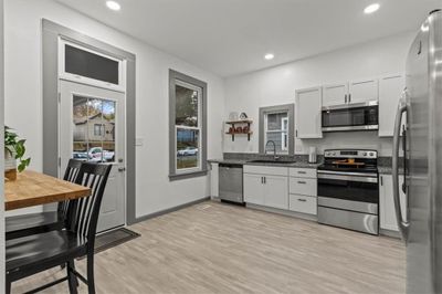 Kitchen featuring light hardwood / wood-style flooring, white cabinetry, sink, dark stone countertops, and appliances with stainless steel finishes | Image 3