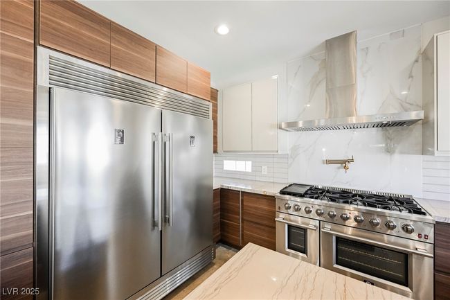 Kitchen with tasteful backsplash, modern cabinets, premium appliances, wall chimney range hood, and light stone counters | Image 16