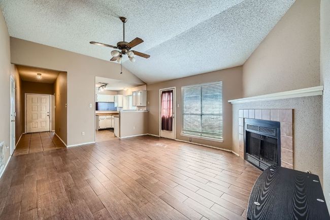 Unfurnished living room with vaulted ceiling, light wood finished floors, ceiling fan, a textured ceiling, and a fireplace | Image 5